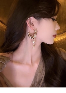 Close-up of elegant gold C-shaped earrings with pearl tassels worn by a model