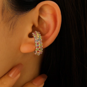 Dettaglio di un ear cuff a forma di C con cristalli colorati e perle indossato sul lobo