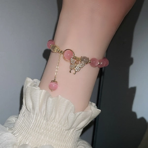 Nahaufnahme von rosa Opal-Perlenarmband mit funkelndem goldenem Schmetterlingsanhänger