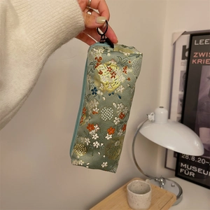 Detail showing traditional floral embroidery on a teal brocade pencil case with metal ring
