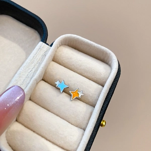 Détail de boucles d'oreilles étoiles asymétriques bleu et orange dans un écrin en velours
