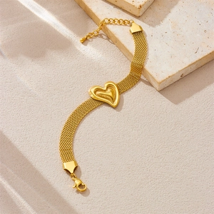 Detail eines goldenen Mesh-Armbands mit 3D-Herzanhänger auf steinerner Oberfläche