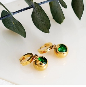 Détail de boucles d'oreilles boules dorées avec zircon cœur émeraude et eucalyptus