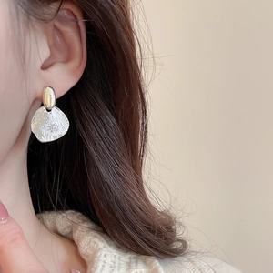 Close-up of fan-shaped silver drop earrings with matte texture on model's ear