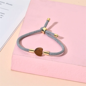 Macro view of adjustable woven gray rope bracelet with heart-shaped tiger eye stone bead
