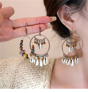 Close-up of bohemian hoop earrings with cowrie shells and beads on a model wearing knitwear