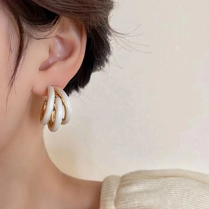 Detail of multi-layered C-shaped earrings with gold plating and white enamel finish