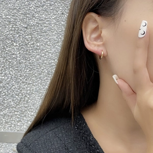 Close-up of minimalist gold hoop earring worn by a model against a neutral background