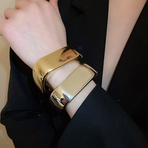 Close-up of polished wide wave bangle bracelets in gold and silver finish on model's wrist