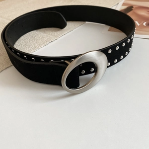 Détail de la ceinture en daim noir avec clous argentés et boucle ovale sur fond minimal