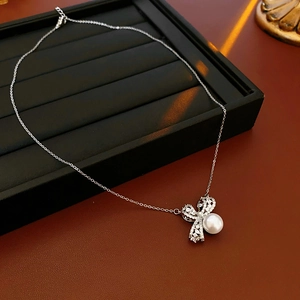 Vue détaillée du collier nœud argenté avec zircon et perle sur plateau noir