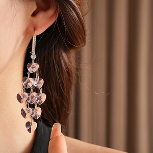 Detail of long tassel earrings with pink heart-shaped stones on model's ear
