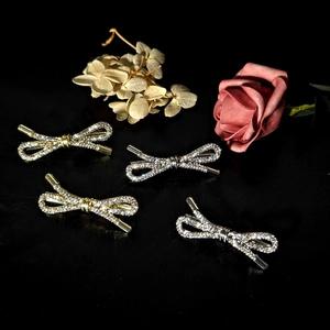 Detail of four crystal bow hairpins in gold and silver finish on a black floral background