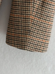 Détail du poignet d'un blazer en tweed avec un motif à carreaux marron, noir et orange