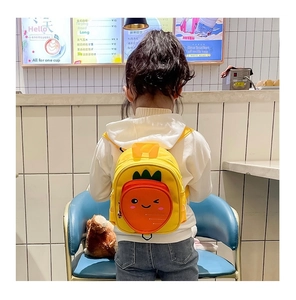 Detail view of a yellow toddler backpack featuring an orange 3D carrot pocket on a model