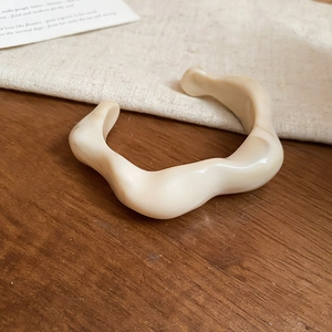 Close-up of cream-colored wavy acrylic open bangle on a natural wooden surface