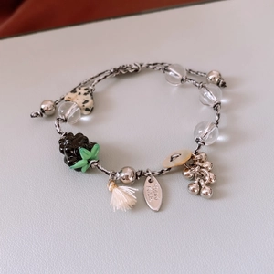 Macro detail of handmade beaded bracelet with heart stone, black berry charm, and tassel