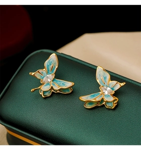 Macro shot of blue enamel butterfly earrings with gold plating on green leather box