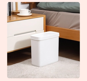 Slim white trash can with vertical texture placed by a wooden bedside table