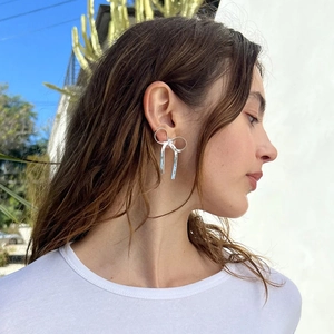 Close-up of a model wearing a silver bow earring with long tassel chain detail