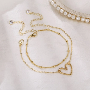 Elegant gold heart pendant bracelet set with bead chain on white silk background
