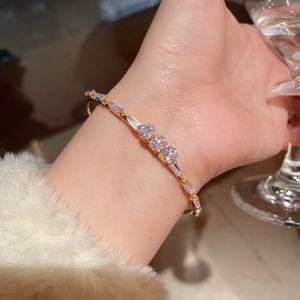 Detail of 18K gold plated bangle with square zircons worn by a wrist near a glass