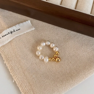 Détail d'une bague en perles d'eau douce et billes dorées sur fond vintage en lin français