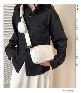 Detailed view of white crossbody bag with heart-embossed texture and small coin pouch