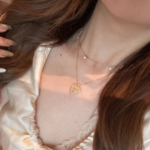 Detail of layered gold heart pendant necklace set with yellow and pink crystals on model