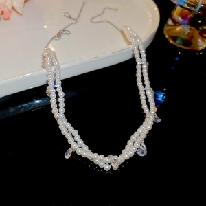 Detailed view of double-layer pearl necklace with teardrop zircon pendant on ceramic dish