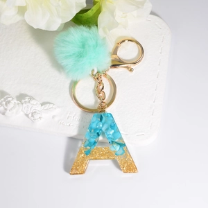 Detail of resin letter A keychain with blue stones, gold glitter, and mint pompom