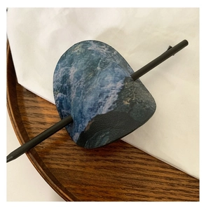 Détail d'un pic à cheveux en cuir bleu avec motif de vagues et tige noire minimaliste