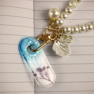 Detail of resin bookmark with purple dried flowers, blue stars and gold leaf pendant