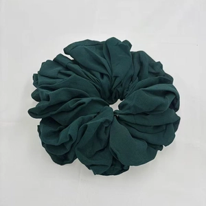Close-up of deep green pleated chiffon hair scrunchie with soft elastic texture on white background