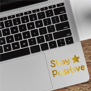 Detail of Stay Positive golden lettering decal applied on a silver laptop surface