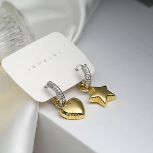 Macro shot of asymmetric gold heart and star charms hanging from silver pavé hoops