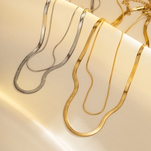 Minimalist gold and silver flat snake bone chain layered necklaces on white silk background