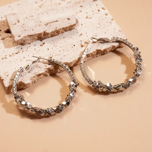 Detail of silver geometric hoop earrings with sparkling sequins on a stone surface