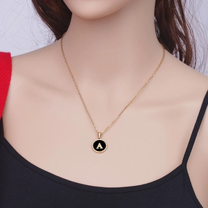 Gros plan d'une chaîne dorée avec pendentif rond noir et lettre A dorée sur un mannequin