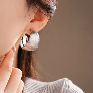 Silver metallic C-shaped hoop earrings with striped texture on female model