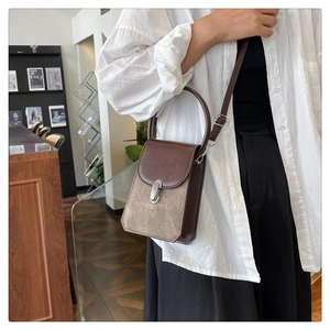 Close-up of brown rectangular crossbody bag with top handle and metal buckle on white shirt
