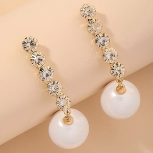 Macro shot of gold drop earrings with five sparkling rhinestones and a white pearl drop