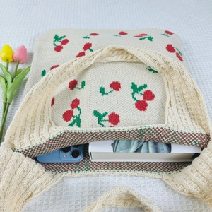 Detail view of large capacity beige knit tote bag with red cherry pattern and tulips