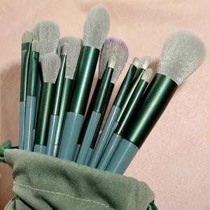 Green makeup brush set with grey bristles in matching fabric pouch on pink silk
