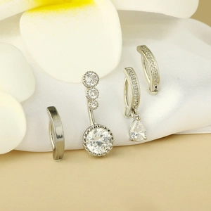 Detailed view of silver stainless steel belly rings with clear zircon on white silk fabric