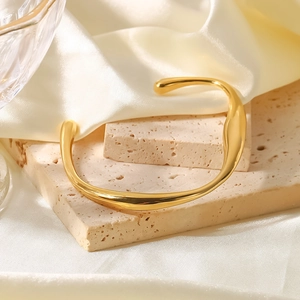 Dettaglio del bracciale rigido ondulato placcato oro 18 carati su una pietra