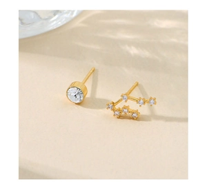 Detailed view of asymmetric gold stud earrings featuring a single gem and zodiac star path