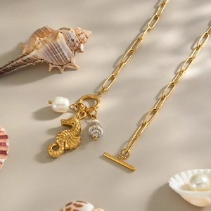 Detail of 18K gold seahorse necklace with pearl and shell charms on beach sand
