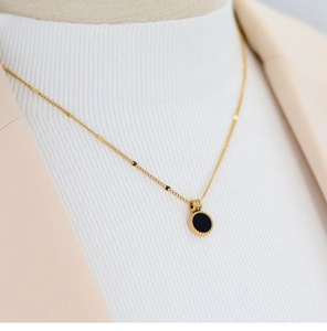 Detail of 18K gold-plated stainless steel necklace with black round pendant on a model