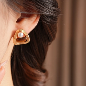 Close-up of vintage golden triangle earrings with white pearl and brown tiger eye stone
